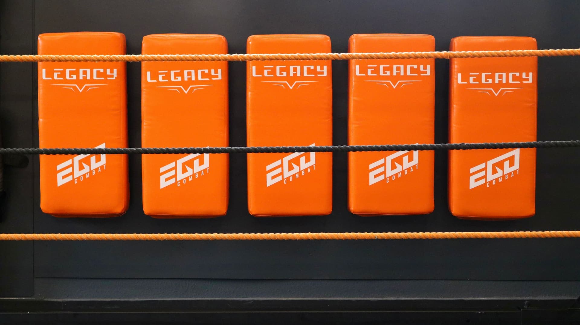 Orange Legacy-Kickschilder an der Wand hinter den Ringseilen in der Striking-Halle in Pinneberg