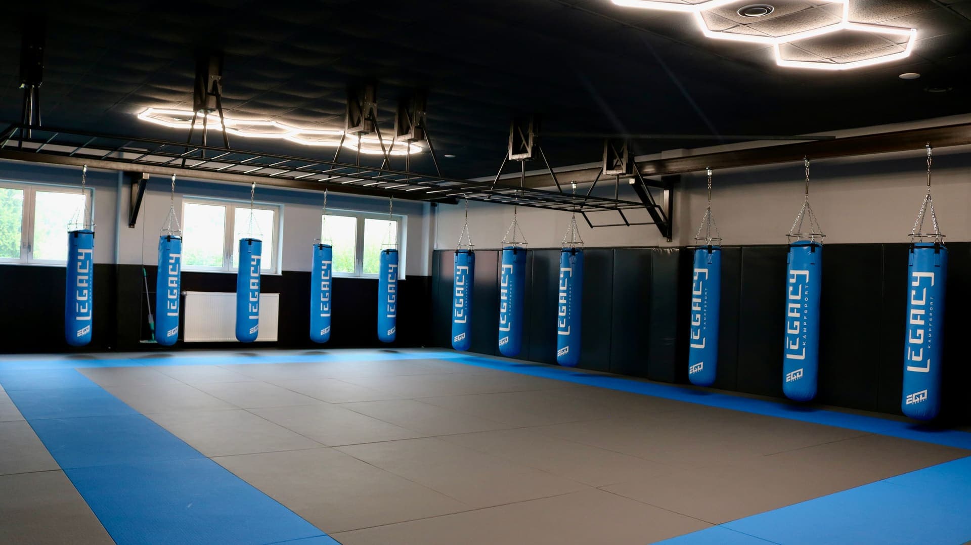 Grappling-Halle von Legacy Kampfsport Pinneberg mit blauer Mattenfläche, Wandprallschutz und Sandsäcken